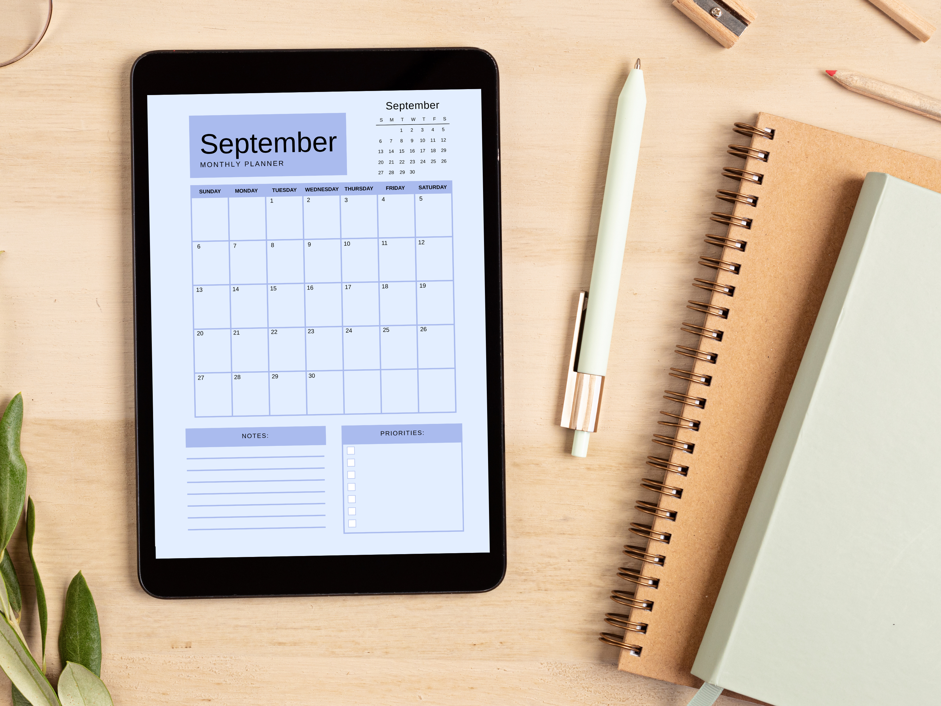 Digital tablet displaying a monthly planner on a wooden surface with a pen and notebook.