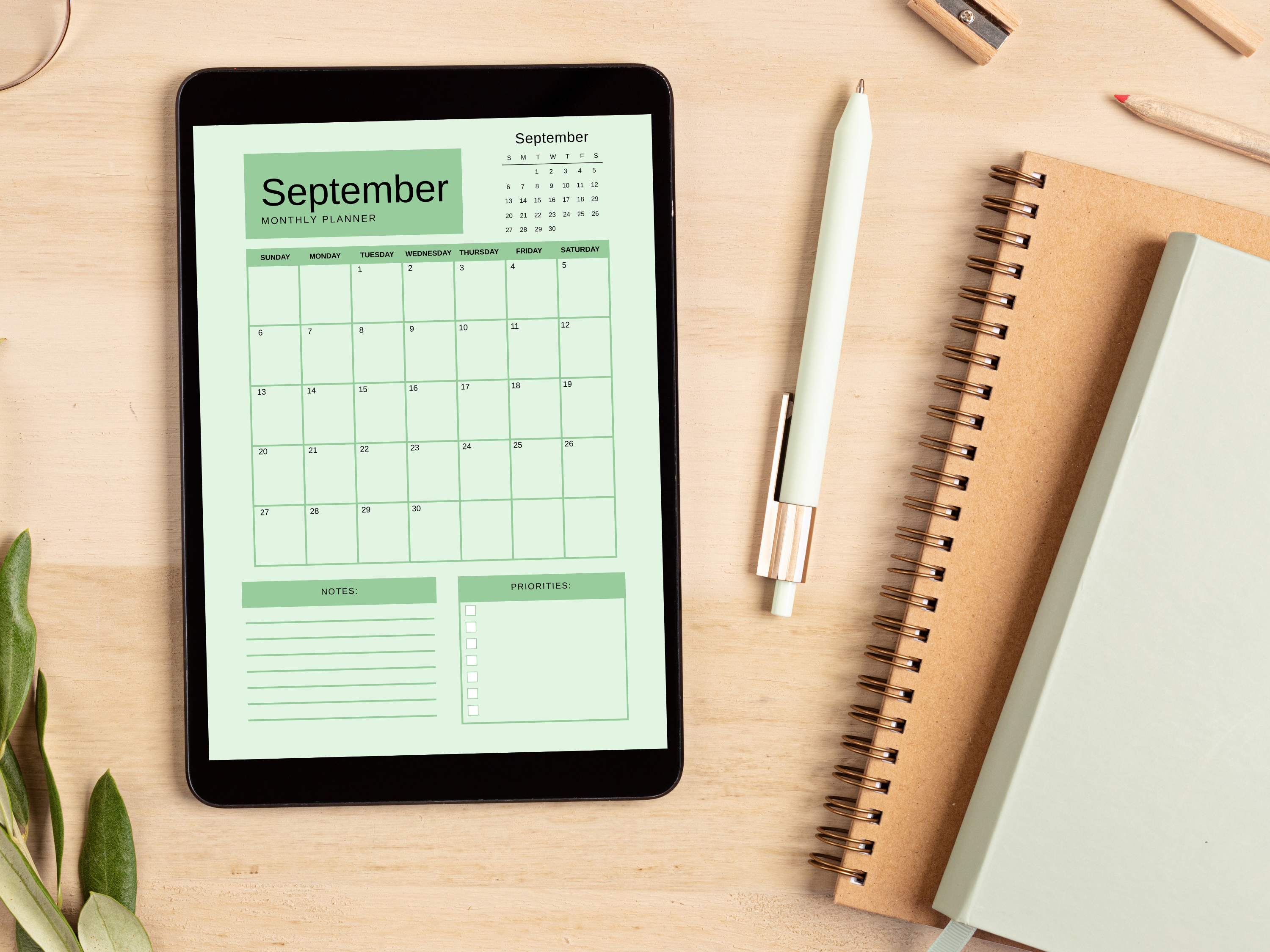 Digital tablet displaying a September planner on a wooden surface with a pen and notebook.