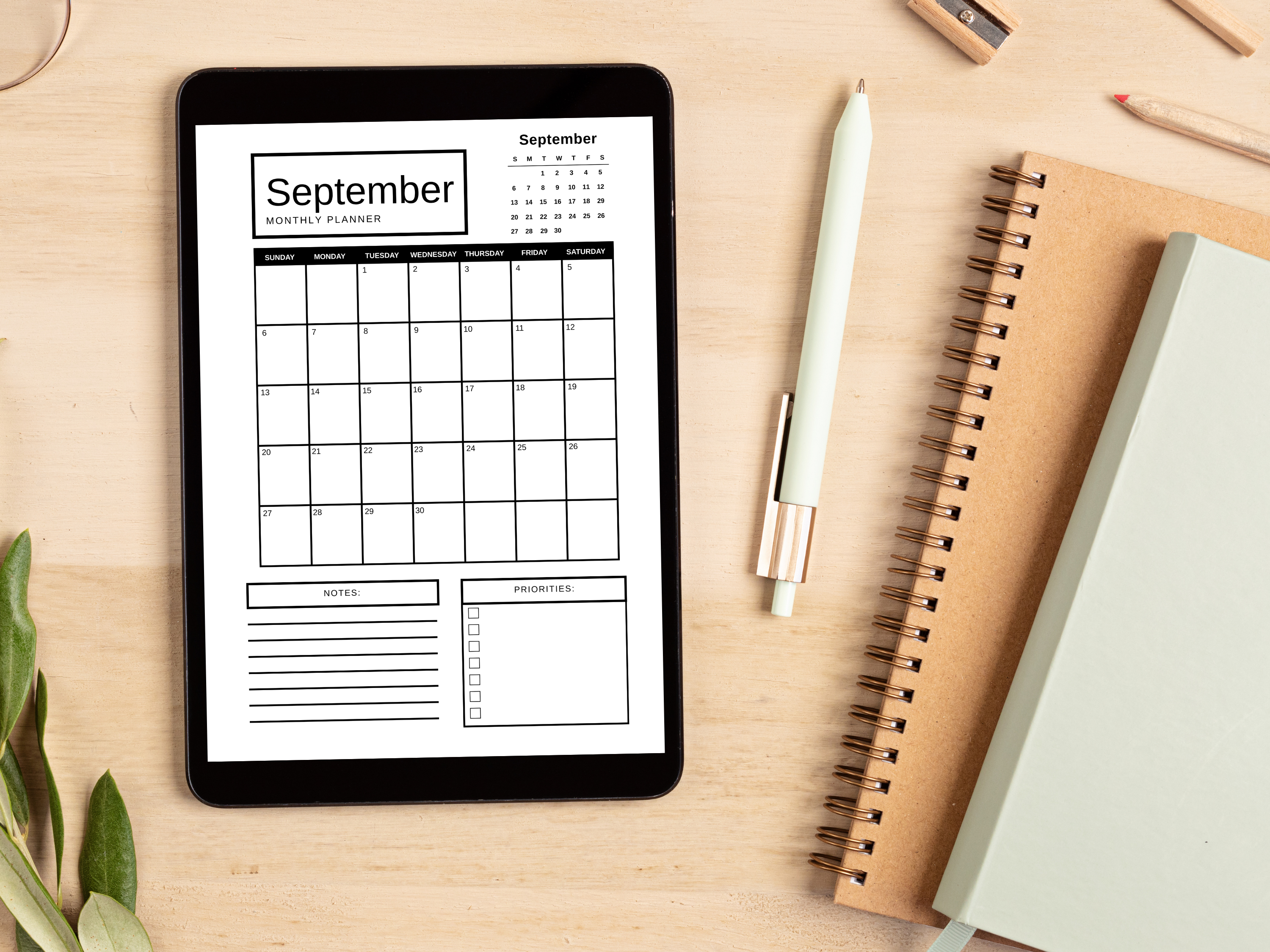 Digital tablet displaying a September planner on a wooden surface with a notebook and pen.