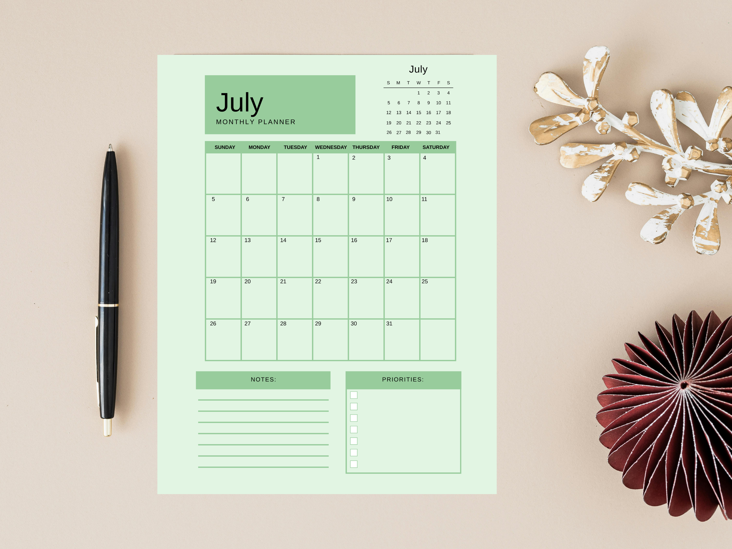 Green monthly planner with a pen and decorative items on a beige background