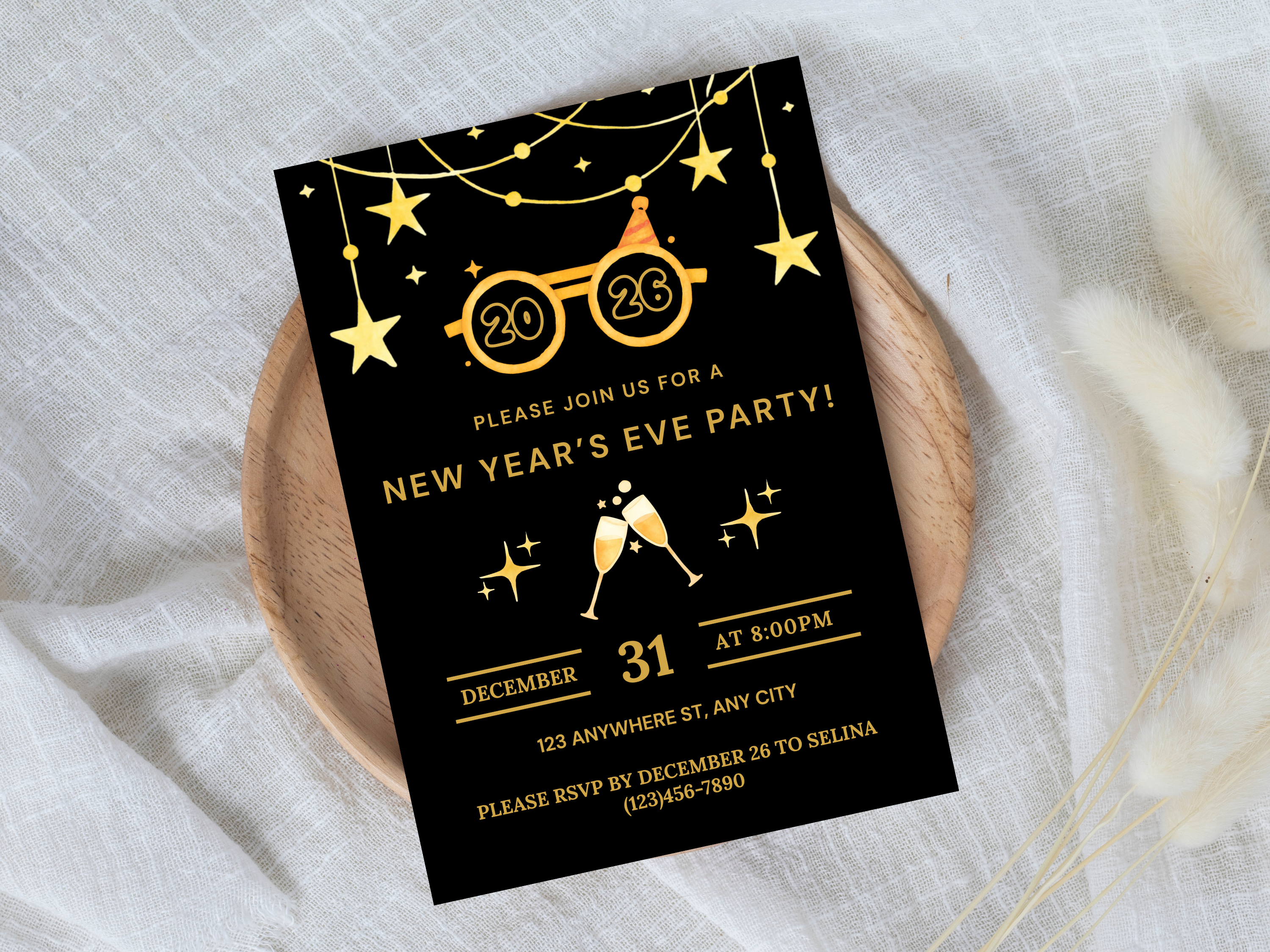 New Year's Eve party invitation card with gold text on a black background, placed on a white fabric surface.