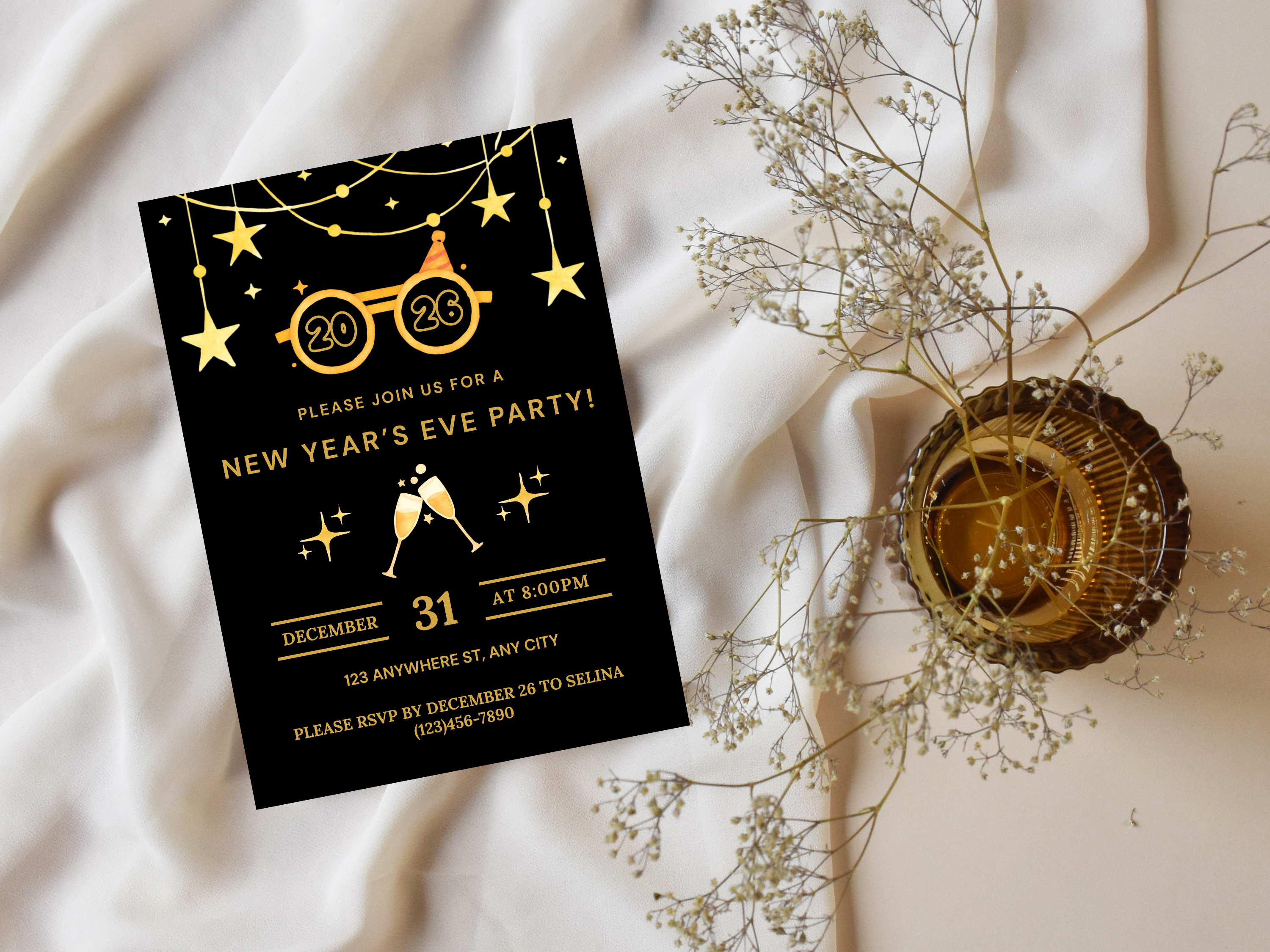 New Year's Eve party invitation card with gold text on a black background, placed on a soft fabric surface with decorative elements.